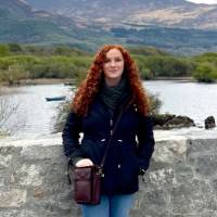 An alum stands against a stone wall with hills in the distance